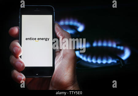 Un homme à la recherche sur le site web logo pour inciter l'entreprise Énergie Énergie sur son téléphone devant sa cuisinière à gaz (usage éditorial uniquement) Banque D'Images