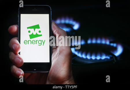 Un homme à la recherche sur le site web logo pour société de l'énergie Énergie OVO sur son téléphone devant sa cuisinière à gaz (usage éditorial uniquement) Banque D'Images