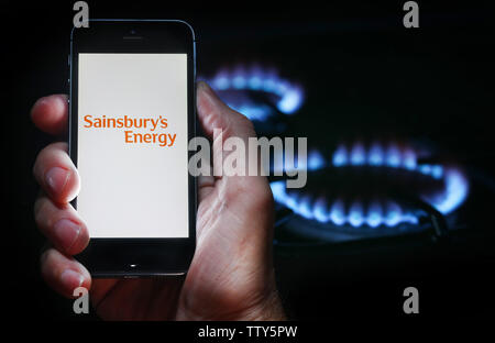 Un homme à la recherche sur le site web logo pour société de l'énergie Énergie Sainsbury's sur son téléphone devant sa cuisinière à gaz (usage éditorial uniquement) Banque D'Images