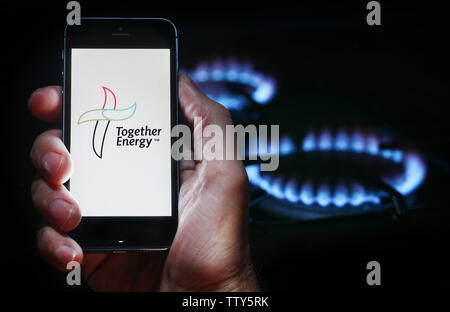 Un homme à la recherche sur le site web logo pour société d'énergie de l'énergie ensemble sur son téléphone devant sa cuisinière à gaz (usage éditorial uniquement) Banque D'Images