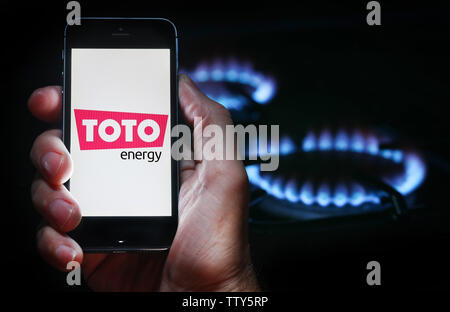 Un homme à la recherche sur le site web logo pour société de l'énergie Énergie Toto sur son téléphone devant sa cuisinière à gaz (usage éditorial uniquement) Banque D'Images