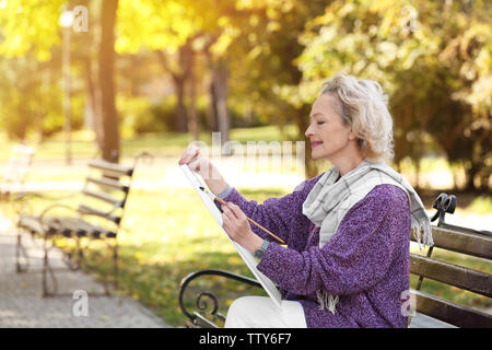 Artiste féminine senior peinture photo tout en restant assis sur un banc dans un beau parc Banque D'Images