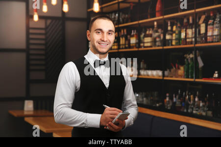 Young handsome waiter avec carnet et un stylo dans le restaurant permanent Banque D'Images