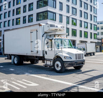 Petit et compact rig semi truck avec réfrigérateur unité le fort la remorque qui transporte des aliments congelés et réfrigérés sur la rue de la ville urbaine à plusieurs niveaux avec b Banque D'Images