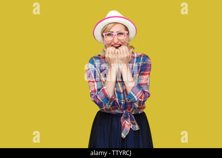 Portrait de triste élégant moderne nerveux mature woman in casual style avec chapeau et lunettes, permanent et des ongles mordant à la caméra et à la panique. je Banque D'Images