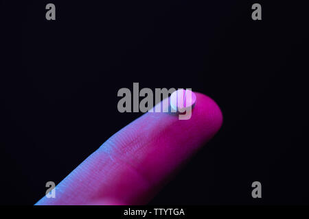 Comprimé sur des doigts. Petit comprimé médicament blanc sur la pointe d'un doigt. Banque D'Images