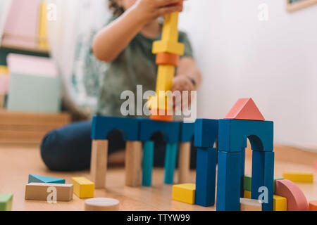 Blocs de construction en bois coloré avec une petite fille à l'arrière-plan flou jouant heureux dans le plancher à la maison ou au jardin, jouets éducatifs fo Banque D'Images