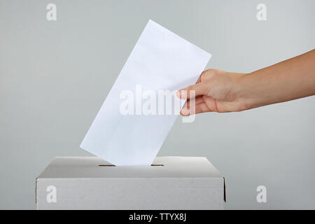 Mettre main de femme dans la boîte de scrutin de vote sur un fond de couleur Banque D'Images