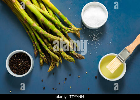 Les asperges prêt à cuire avec sel, poivre et l'huile d'olive sur fond bleu Banque D'Images