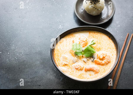 Tom Yam kung soupe thaï aux crevettes, fruits de mer, le lait de coco, le piment et le riz en noir bol. Close up. La cuisine asiatique. Banque D'Images