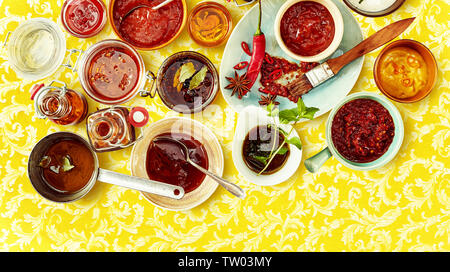Vue aérienne de chutney rouge et la salsa avec d'autres condiments rouge dans des bols sur jaune fond à motifs Banque D'Images