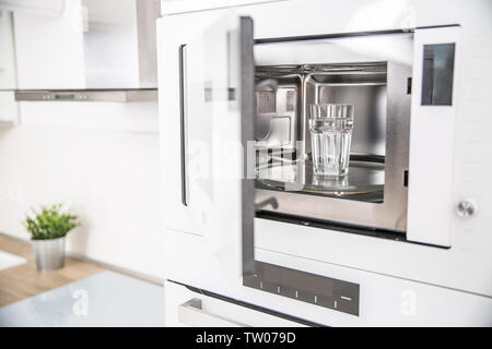 Four à micro-ondes encastré dans la cuisine avec une tasse d'eau pure. Banque D'Images