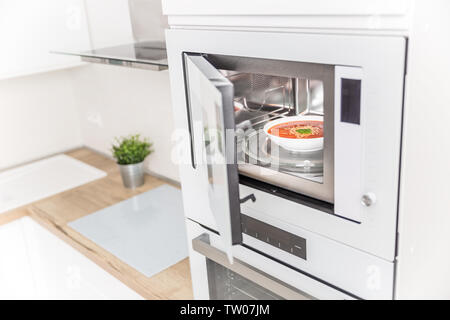 Four à micro-ondes encastré dans la cuisine avec la soupe aux tomates en plaque blanche. Banque D'Images