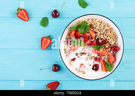 Petit-déjeuner sain - granola, fraises, cerises, noix et le yogourt dans un bol sur une table en bois. La nourriture végétarienne. concept Vue d'en haut Banque D'Images