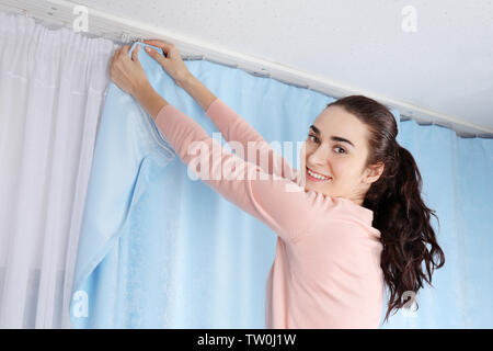 Jeune femme d'installer des rideaux sur fenêtre Banque D'Images