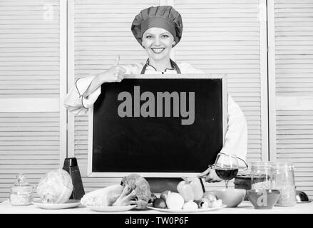 En donnant son approbation. Pretty woman gesturing Thumbs up avec tableau noir vide. Maître cuisinier du Cours de cuisine. Le cuisinier en chef l'enseignement en école de cuisine. Classe de maître en école hôtelière, copiez l'espace. Banque D'Images