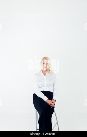 Studio portrait d'une femme d'affaires blonde attrayant dans une chemise blanche et un pantalon noir contre blanc fond uni Banque D'Images