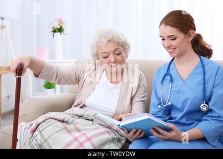 Infirmière lisant livre pour personnes âgées woman on couch Banque D'Images