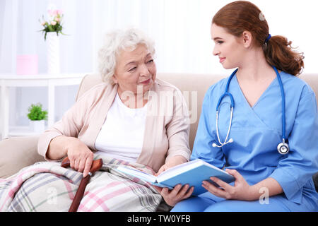Infirmière lisant livre pour personnes âgées woman on couch Banque D'Images