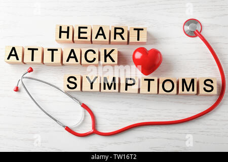 Les symptômes d'une crise cardiaque texte faite de cubes et de stéthoscope sur fond de bois Banque D'Images