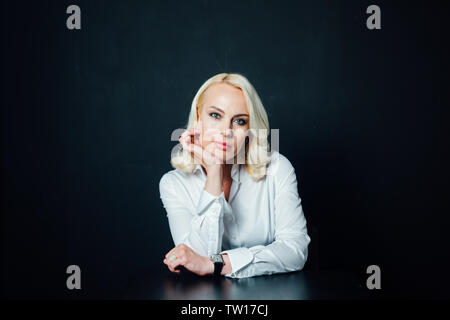 Studio portrait d'une femme d'affaires blonde attrayant dans une chemise blanche et un pantalon noir contre fond uni Banque D'Images