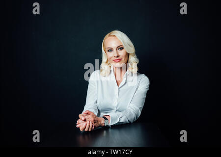 Studio portrait d'une femme d'affaires blonde attrayant dans une chemise blanche et un pantalon noir contre fond uni Banque D'Images