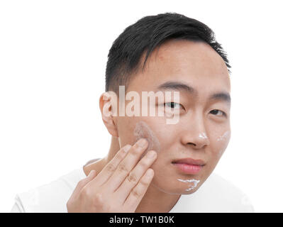 Young Asian man l'application de la crème pour les peaux à problèmes sur une face, sur fond blanc Banque D'Images