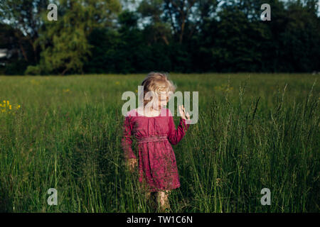 Beau mignon adorable preschool Caucasian girl walking in tall grass prairie haute sur au coucher du soleil. Heureux l'enfant kid profitant de l'été. Authentique de vie Banque D'Images