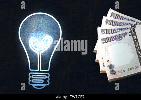 Glowing lightbulb with bundles of hundred rupees banknotes Stock Photo