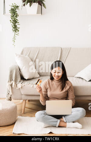 Happy Girl Faire les paiements en ligne par carte de crédit et l'ordinateur portable, Sitting on Floor Banque D'Images