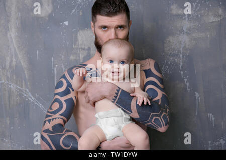 Beau jeune homme tatoué holding cute little baby sur fond gris Banque D'Images