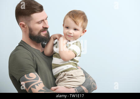 Beau jeune homme tatoué holding cute little boy sur fond clair Banque D'Images