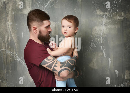 Beau jeune homme tatoué holding cute little boy sur fond gris Banque D'Images