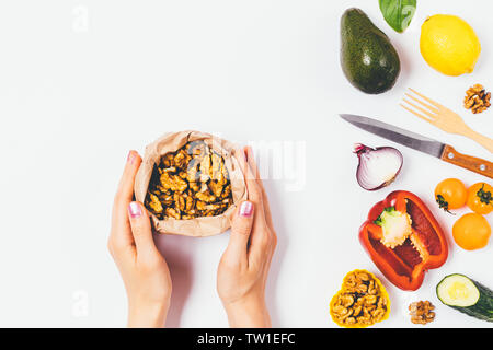 Vue d'en haut les mains tenant un sac en papier avec des noix à côté de légumes frais et le couteau avec une fourchette. Concept de saine alimentation avec des gras insaturés. Banque D'Images