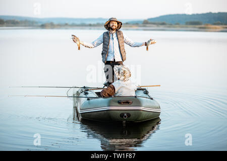 Happy man holding des poissons fraîchement pêchés en étant debout sur le bateau avec son grand-père sur le lac tôt le matin Banque D'Images