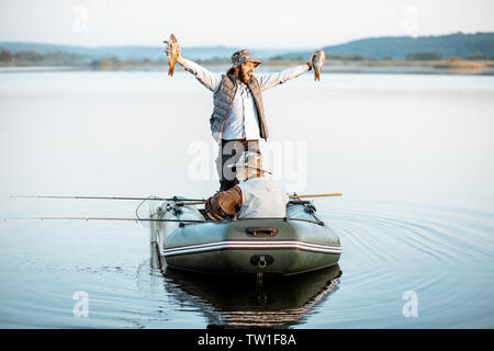 Happy man holding des poissons fraîchement pêchés en étant debout sur le bateau avec son grand-père sur le lac tôt le matin Banque D'Images