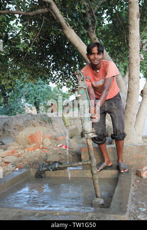 Un adolescent tirant de l'eau de la pompe à eau, Inde Banque D'Images