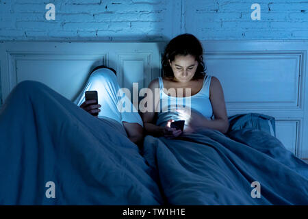 Sad man and woman couple marié en utilisant leur téléphone mobile intelligent au lit la nuit ignorant les uns les autres comme des étrangers dans la relation et la communication pro Banque D'Images