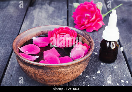 Près de l'huile essentielle de pétales de rose rouge bol avec sur un fond en bois sombre. L'aromathérapie. Banque D'Images