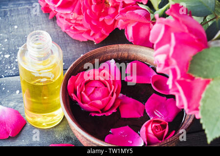 Près de l'huile essentielle de pétales de rose rouge bol avec sur un fond en bois sombre. L'aromathérapie. Banque D'Images