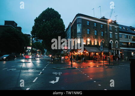 Une pub dans la soirée avec feu orange à une intersection dans les rues de Londres, au Royaume-Uni. Sur le côté gauche sont les bus rouges typiques. Banque D'Images