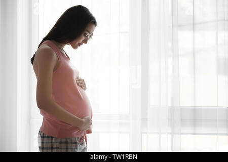 Belle femme enceinte, debout près de fenêtre à la maison Banque D'Images