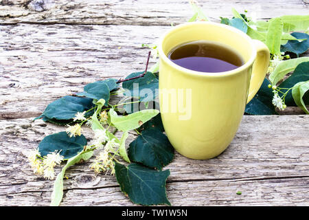 Linden du thé dans une tasse jaune se trouve près de fleurs de tilleul dans le contexte des anciennes cartes. Thé de fines herbes avec des fleurs de tilleul. Banque D'Images