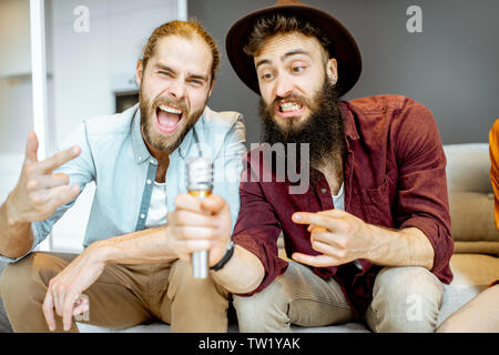 Deux amis chanter fort avec microphone karaoke tout en jouant à la maison Banque D'Images