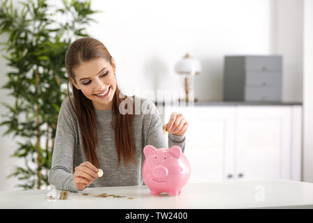 Belle jeune femme mettre des pièces dans la tirelire à la maison Banque D'Images