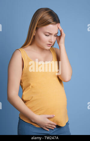 Femme enceinte souffrant de maux de tête sur fond bleu Banque D'Images