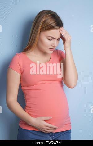 Femme enceinte souffrant de maux de tête sur fond bleu Banque D'Images