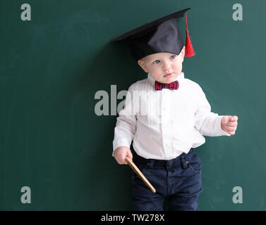 Cute little boy avec l'aiguille et magister hat près de tableau noir Banque D'Images