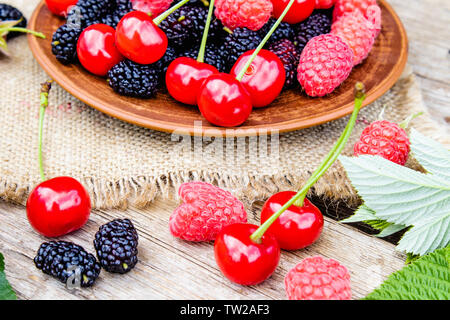 Fruits des framboises, cerises, mûres dans un bol sur fond de bois et de toile. Close-up Banque D'Images