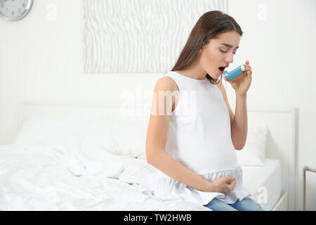 Jeune femme enceinte à l'aide d'asthme au cours de l'inhalateur à la maison Banque D'Images